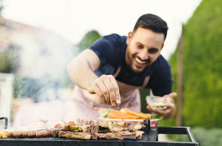 man seasoning grill cooking meat and vegetables