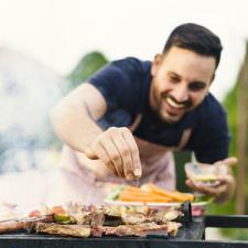 man seasoning grill cooking meat and vegetables